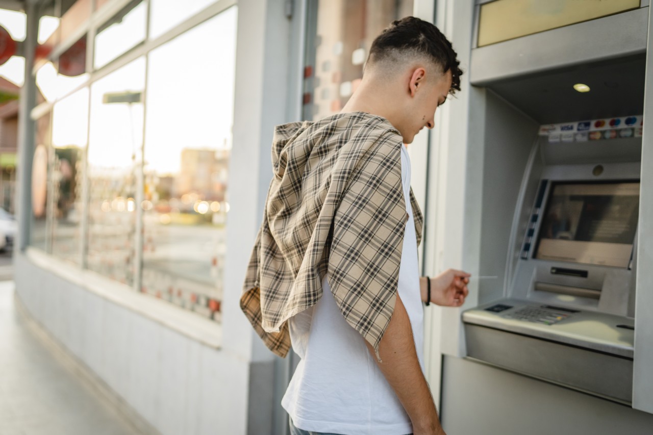 man teenage student using credit card and withdraw cash at the ATM man teenage student using credit card and withdrawing cash at the ATM