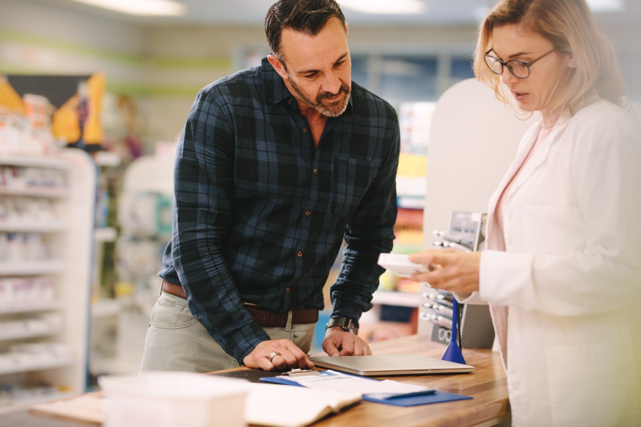 Pharmacist showing medicine to customer in pharmacy Female pharmacist showing medicine to male customer in pharmacy. Chemist suggesting medical drug to buyer in pharmacy drugstore.